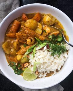 Prawn massaman curry served with rice, herbs, peanuts, and lime.